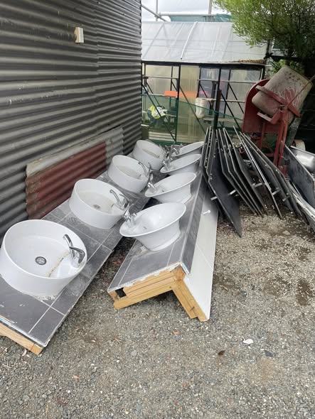 Row of modern white hand basins outdoors against corrugated iron